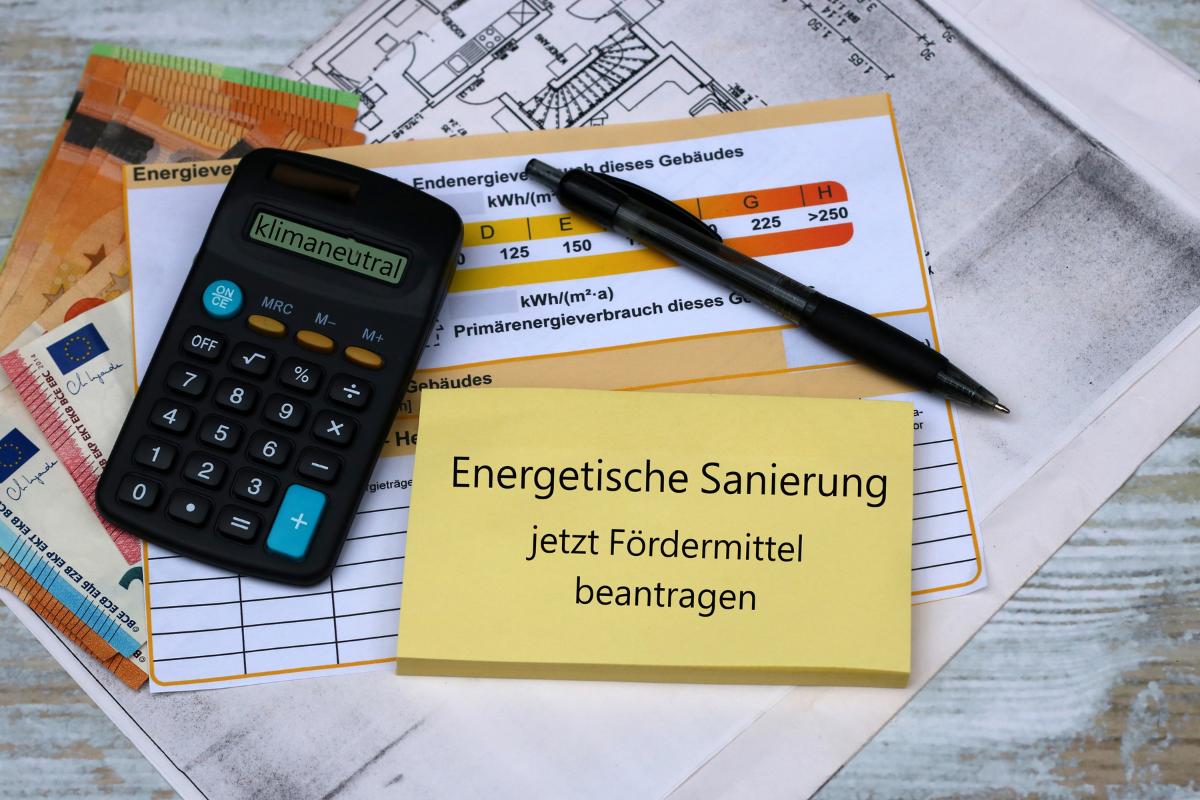 Auf einem Tisch liegen Geldscheine, ein Taschenrechner und Kugelschreiber sowie ein Dokument zur Eintragung des Energieverbrauchs eines Hauses und ein Zettel auf dem steht: Energetische Sanierung jetzt Fördermittel beantragen.